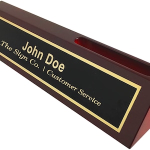 May include: A mahogany desk nameplate with a black plaque and gold lettering. The nameplate reads "John Doe, The Sign Co. | Customer Service".