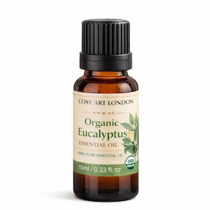 Puede incluir: Un frasco pequeño de vidrio ámbar de aceite esencial de eucalipto orgánico Cosy Art London con tapa negra estriada. La etiqueta muestra texto verde, una ilustración botánica de hojas de eucalipto, 10 ml / 0,33 fl. oz. y USDA Organic.