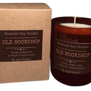 May include: A brown glass candle with a white wax interior and a wick, next to a matching cardboard box. The candle and box feature a label that reads "Bookish Soy Candle OLD BOOKSHOP" with text about dusty tomes and leather-bound books.