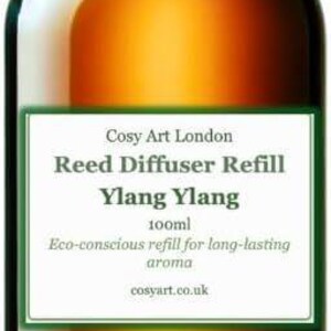 May include: A 100ml amber glass bottle with a black cap containing Ylang Ylang reed diffuser refill. The white label features the text: Cosy Art London, Reed Diffuser Refill, Ylang Ylang, 100ml, Eco-conscious refill for long-lasting aroma, cosyart.co.uk.