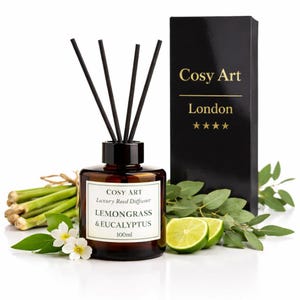 Puede incluir: Un difusor de varillas de vidrio ámbar de 100ml con varillas negras, etiquetado como Cosy Art Luxury Reed Diffuser Lemongrass & Eucalyptus. Junto a él hay una caja negra con el texto dorado Cosy Art London y cuatro estrellas.