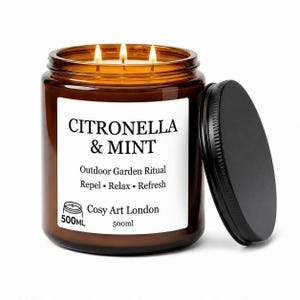 Puede incluir: Una vela en frasco de vidrio ámbar de 500ml con tres mechas encendidas y una tapa de metal negra. La etiqueta blanca dice CITRONELLA & MINT, Outdoor Garden Ritual, Repel • Relax • Refresh y Cosy Art London. La cera emite una luz cálida.