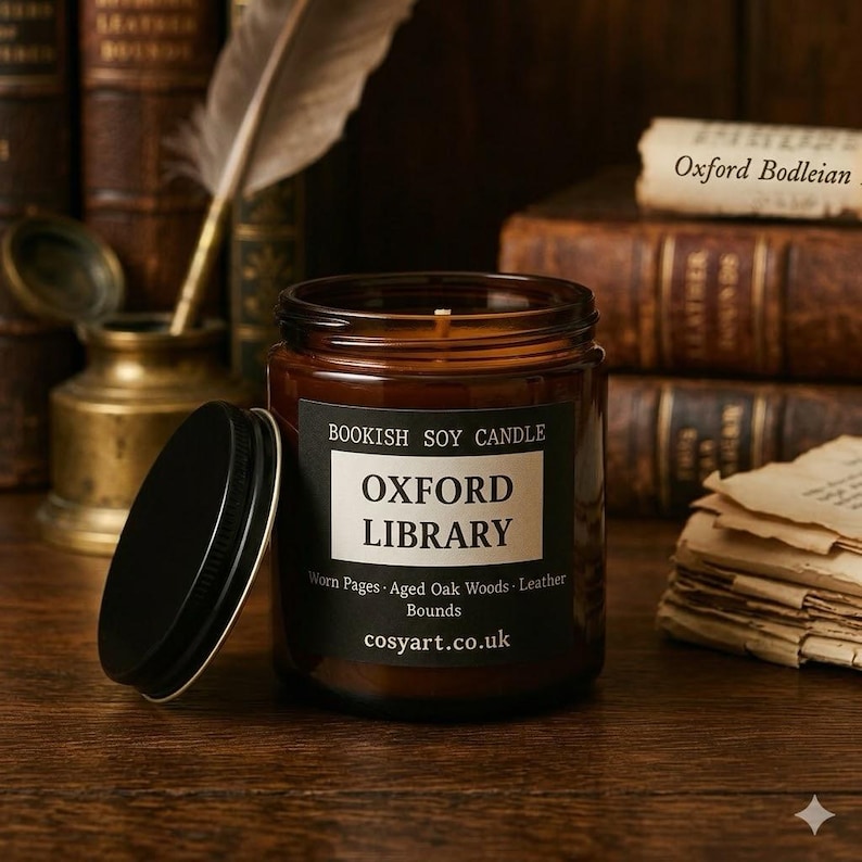 May include: A brown glass jar candle with a black lid, labeled "Oxford Library." The label includes the text "Bookish Soy Candle" and "Worn Pages, Aged Oak Woods, Leather Bounds." The candle sits on a wooden surface, with books in the background.