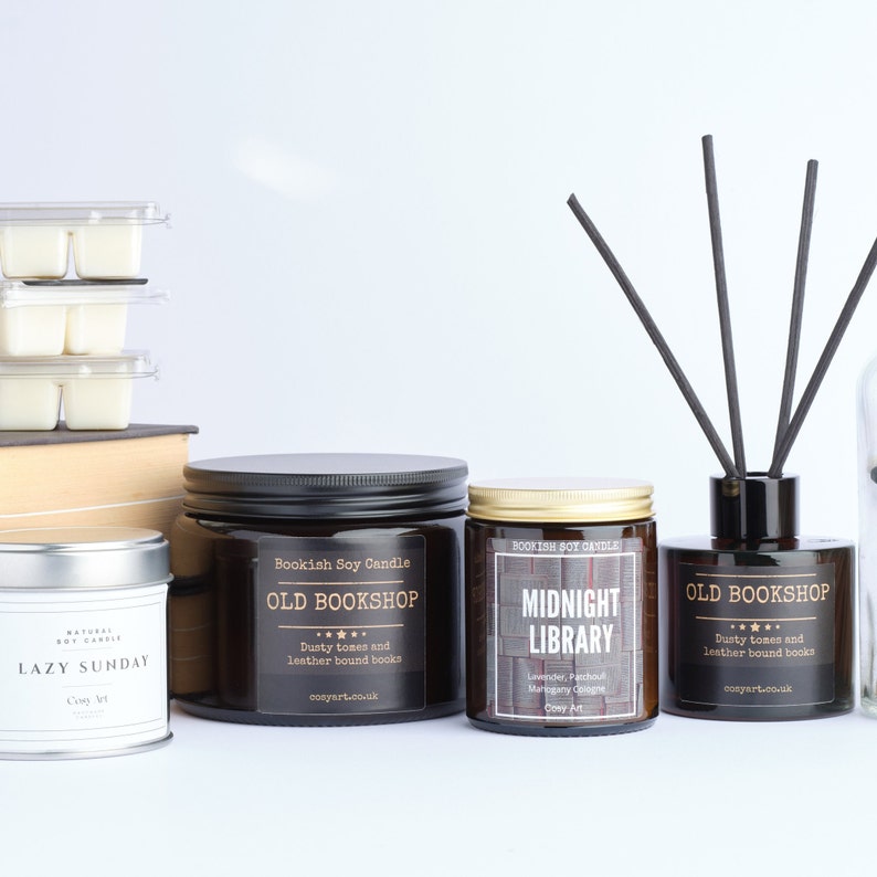Puede incluir: Tres tarros de velas de vidrio marr&oacute;n con tapas negras y etiquetas doradas. Las velas est&aacute;n etiquetadas como "Old Bookshop", "Midnight Library" y "Old Bookshop". Las velas est&aacute;n dispuestas en una fila sobre una superficie blanca. Hay una caja marr&oacute;n y una pila de fundidos de cera blanca detr&aacute;s de las velas. Un difusor de vidrio negro con ca&ntilde;as negras est&aacute; a la derecha de las velas.