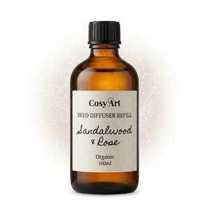 Puede incluir: Un frasco de vidrio ámbar de 100ml con tapón de rosca negro que contiene aceite de recarga para difusor de varillas. La etiqueta de color blanco roto presenta el texto Cosy Art, REED DIFFUSER REFILL, Sandalwood & Rose y Organic 100ml en negro.