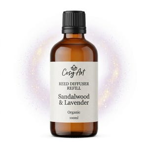 May include: An amber glass bottle with a black cap containing 100ml of reed diffuser refill. The white label features the text Cosy Art, Reed Diffuser Refill, Sandalwood & Lavender, and Organic. A glowing purple light effect surrounds the bottle.