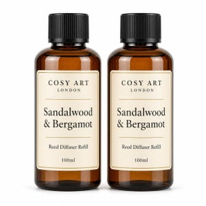 Pode incluir: Dois frascos de vidro âmbar com tampas de rosca pretas estriadas, cada um contendo 100ml de líquido. Os rótulos dizem COSY ART LONDON, Sandalwood & Bergamot e Reed Diffuser Refill. Os frascos são idênticos em forma, tamanho e design de rótulo.