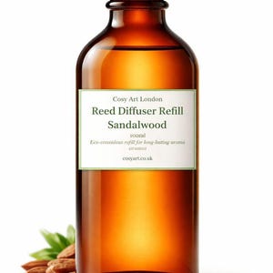Puede incluir: Una botella de vidrio ámbar con tapa de rosca negra que contiene 100ml de recambio de difusor de varillas de sándalo. La etiqueta blanca presenta el texto Cosy Art London, Reed Diffuser Refill, Sandalwood, 100ml, Eco-conscious refill for long-lasting aroma y cosyart.co.uk.