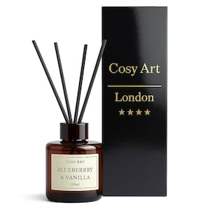 May include: A 100ml amber glass reed diffuser bottle with four black reeds and a cream label reading Cosy Art BLUEBERRRY & VANILLA. Beside it stands a tall, rectangular black box featuring the gold text Cosy Art London and four gold stars.