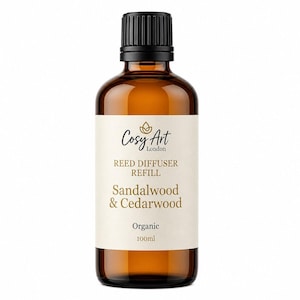 May include: A 100ml amber glass bottle with a black screw cap containing a reed diffuser refill. The label features the text Cosy Art London, REED DIFFUSER REFILL, Sandalwood & Cedarwood, and Organic in black and gold lettering on a cream background.