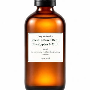 Könnte beinhalten: Eine bernsteinfarbene Glasflasche mit schwarzem Schraubverschluss, die 100ml Nachfüllflüssigkeit für einen Raumduft enthält. Das weiße Etikett trägt den Text: Cosy Art London, Reed Diffuser Refill, Eucalyptus & Mint, 100ml, An energising refill for long-lasting aromas, cosyart.co.uk.