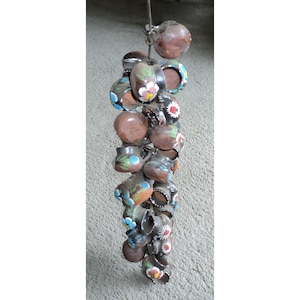 May include: A string of small, brown clay pots with painted floral designs in shades of blue, pink, and white. The pots are strung together with a metal wire and hang from a ceiling.