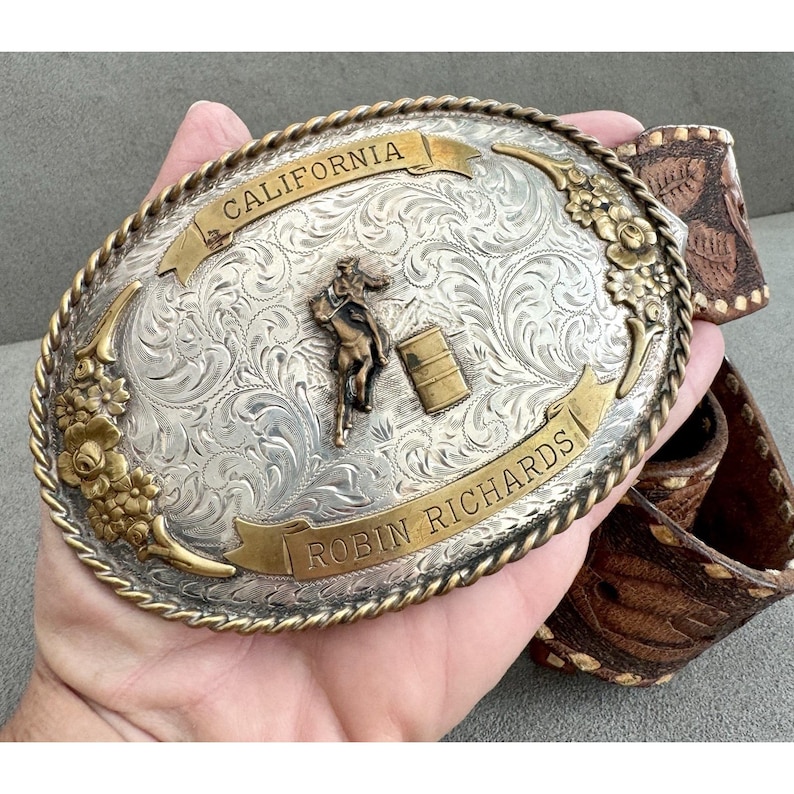 Puede incluir: Una taza de cer&aacute;mica blanca con asa negra y el texto "But First, Coffee" en negrita negra. La taza se encuentra sobre un fondo borroso, sugiriendo un ambiente acogedor.