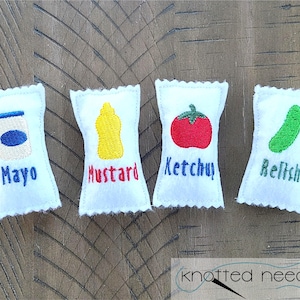 May include: Four white felt pouches with embroidered images and text. The pouches are labeled "Mayo", "Mustard", "Ketchup", and "Relish".