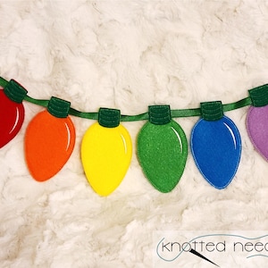 May include: A colourful felt garland of light bulbs in red, orange, yellow, green, blue, and purple. The garland is strung on a green ribbon.