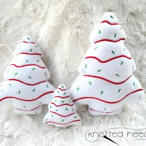 以下が含まれることがあります： 赤と緑の刺繍が施された白いぬいぐるみ製のクリスマスツリーのオーナメントが3つ。一番大きなツリーは約25cm、真ん中のツリーは約15cm、一番小さなツリーは約10cmです。