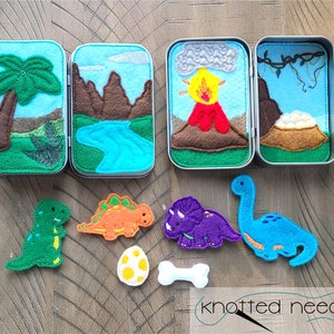 May include: A set of felt dinosaur play pieces in a tin box. The box has four compartments with felt scenes of a palm tree, a river, a volcano, and a cave. The dinosaur pieces include a green T-Rex, an orange Stegosaurus, a purple Triceratops, and a blue Brachiosaurus.
