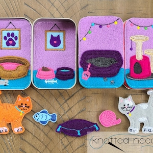 Könnte beinhalten: Filz-Spielset für ein Katzen-Filzbrett. Das Set enthält ein Katzenbett, eine Katzentoilette, einen Kratzbaum, eine Futterschale, einen Fisch, eine Katze, ein Wollknäuel und eine lila Matte. Das Set ist in einem lila, rosa, braunen und blauen Farbschema gehalten.