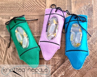 May include: Three felt crayon-shaped bags with clear plastic windows. The bags are filled with small sweets and have black drawstrings. The bags are green, purple, and blue.