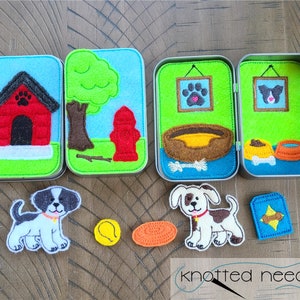 Könnte beinhalten: Filz-Spielset mit einem Hundehaus, einem Hydranten, einem Hundebett, einer Hundenapf, einem Knochen und zwei Hunden. Das Set befindet sich in einer Blechdose mit grünem Hintergrund und blauem Rand. Die Hunde sind weiß mit schwarzen Flecken.
