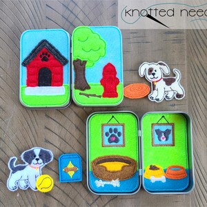 May include: A set of felt play scenes in a tin box, featuring a dog, a doghouse, a fire hydrant, a tree, a bowl of food, a bone, a dog bed, and a picture frame with a paw print. The set is perfect for imaginative play and storytelling.