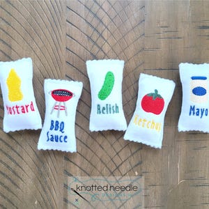 May include: Five white rectangular felt patches with scalloped edges, each featuring embroidered food icons and text. The designs include a yellow mustard bottle, a red BBQ grill, a green pickle, a red tomato, and a blue and white mayo jar.