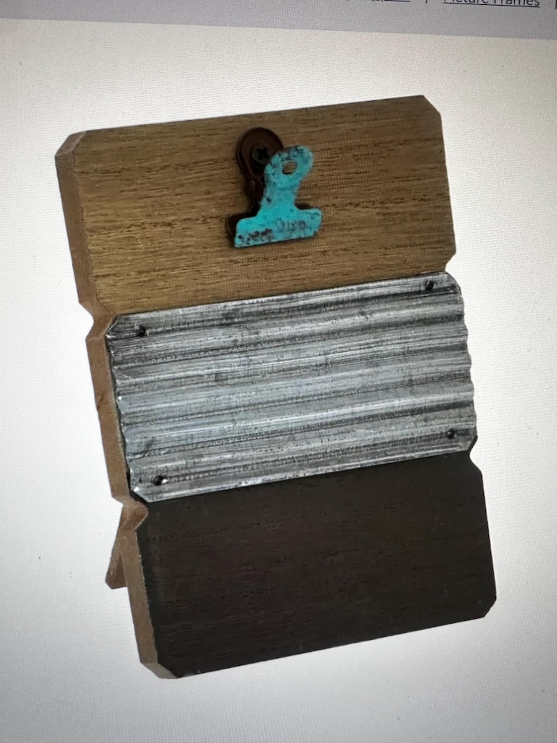 Puede incluir: Un marco de fotos r&uacute;stico de madera con un clip turquesa. El marco tiene una secci&oacute;n superior de madera marr&oacute;n claro, una secci&oacute;n media de metal corrugado y una secci&oacute;n inferior marr&oacute;n oscuro. El marco est&aacute; dise&ntilde;ado para colocarse de pie.