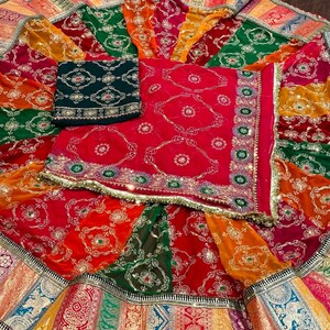 May include: A colorful, multi-layered skirt with a green, red, and gold patterned design. The skirt has a decorative border with gold and silver accents. The skirt is made of a sheer fabric and has a flowing silhouette.