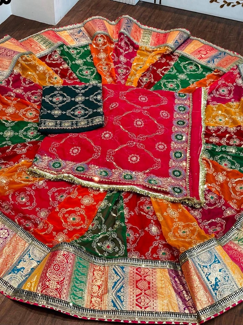 May include: A colorful, multi-layered skirt with a green, red, and gold patterned design. The skirt has a decorative border with gold and silver accents. The skirt is made of a sheer fabric and has a flowing silhouette.