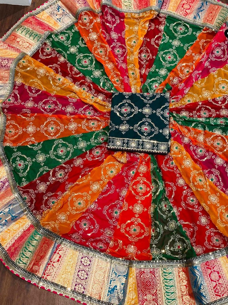 May include: A colorful circular skirt with a green embroidered top. The skirt has a multi-colored border with gold accents. The skirt is made of a sheer fabric with a floral pattern.