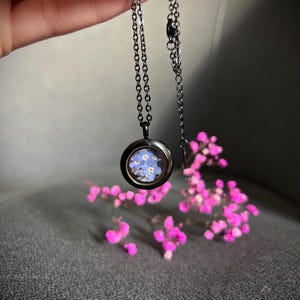 May include: A silver chain necklace with a round pendant featuring a pressed forget-me-not flower design.
