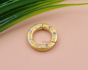 May include: A gold-toned ring with a circular design and clear stones set around the edge. The ring is open on one side and has a hinge closure. The text "ANSHLI JEWELS" is visible on the ring.
