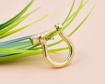 Pode incluir: Fecho em forma de U de metal dourado com borda arredondada. O fecho está sobre um fundo verde.