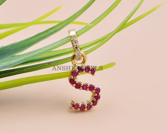 May include: Gold pendant charm in the shape of the letter S, encrusted with small red gemstones and a few clear gemstones.