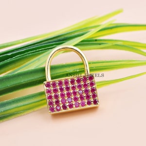 May include: Gold padlock charm with a red ruby stone design. ANSHIL JEWELS is printed on the charm.