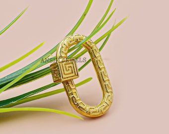 May include: Gold-toned metal clasp with a geometric pattern. The clasp is oval-shaped and has a square latch with a similar geometric pattern.