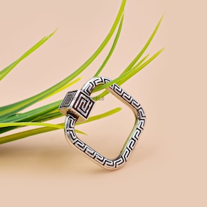 May include: A silver square-shaped ring with a geometric design. The ring is made of sterling silver and has a Greek key pattern.