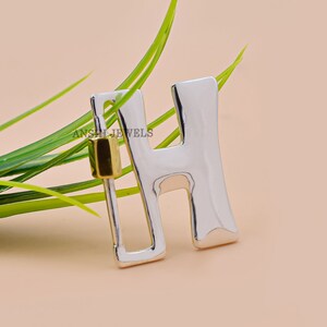 Pode incluir: Encanto de letra H em prata e ouro. O encanto tem a forma da letra H e um acabamento prateado brilhante. O encanto tem um acento dourado na parte superior.