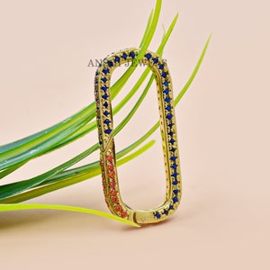 May include: Gold-toned metal clasp with a rectangular shape. The clasp is decorated with blue and orange gemstones.