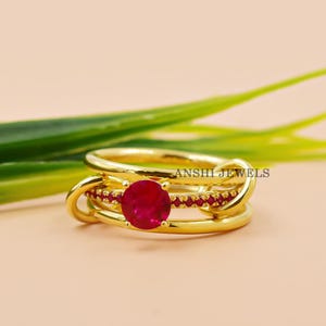 May include: Gold ring with a red ruby gemstone and smaller red ruby stones set in the band. The ring is designed with a twisted band.