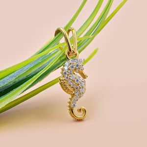 May include: A gold-tone seahorse pendant with clear cubic zirconia stones. The pendant is hanging from a green plant.