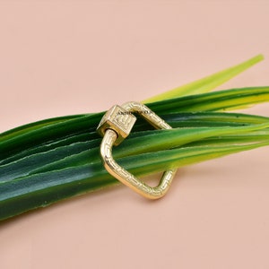 May include: Gold-toned metal square-shaped clasp with a decorative design. The clasp is on a green background.