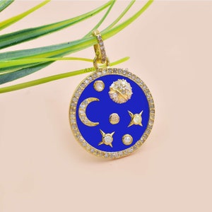 May include: Gold pendant necklace with a blue enamel circle featuring a crescent moon, stars, and a small round stone set with diamonds. The circle is surrounded by a row of diamonds.