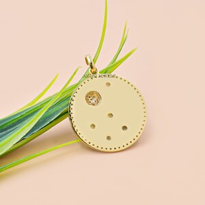 May include: Gold pendant with a circular design featuring a small circle in the center and a constellation of small dots around it. The pendant has the text "ANSHI JEWELS" engraved on the back.