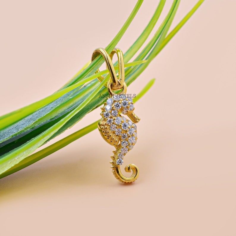 May include: A gold-tone seahorse pendant with clear cubic zirconia stones. The pendant is hanging from a green plant.
