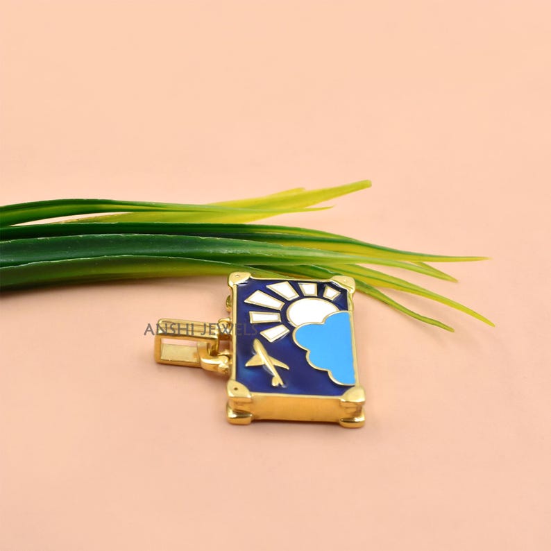 May include: A rectangular gold-tone pendant featuring an enamel inlay of a dark blue sky with a white sun, a light blue cloud, and a small gold airplane. The pendant has a gold bail on the left side and the text ANSHI JEWELS is visible on the surface.