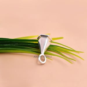 K&ouml;nnte beinhalten: Eine polierte, silberfarbene Schmuck&ouml;se aus Metall mit einem konisch zulaufenden, facettierten geometrischen K&ouml;rper und einer runden &Ouml;se an der Basis. Das Bauteil hat eine glatte, reflektierende Oberfl&auml;che und liegt auf gr&uuml;nen Halmen. Der Text ANSHI JEWELS ist sichtbar.