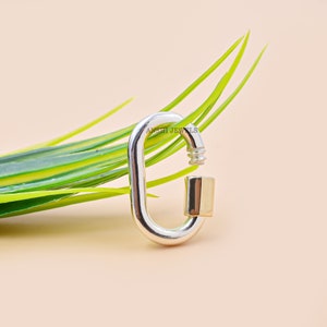 May include: A silver and gold oval-shaped clasp with a spring-loaded gate. The clasp is made of metal and has a polished finish. The clasp is a popular accessory for jewellery making and can be used to connect chains, bracelets, and other jewellery pieces.