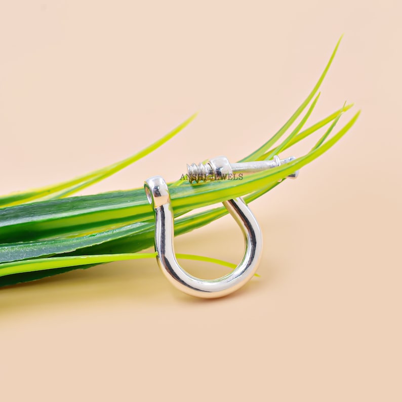 May include: Silver-toned metal clasp with a screw closure. The clasp is lying on a bed of green grass.