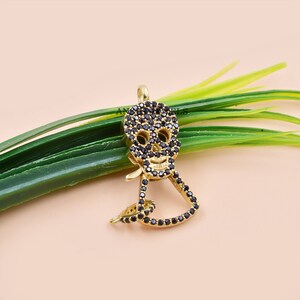 Puede incluir: Charme de colgante de calavera en tono dorado con piedras de circonita c&uacute;bica negras. La calavera est&aacute; detallada con cuencas de los ojos, una nariz y una boca.